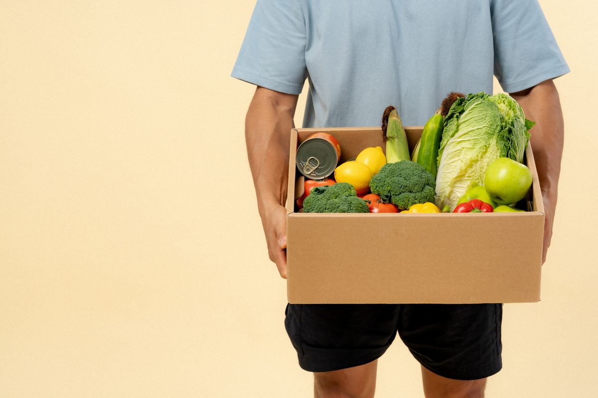 Person carrying a box of fresh vegetables